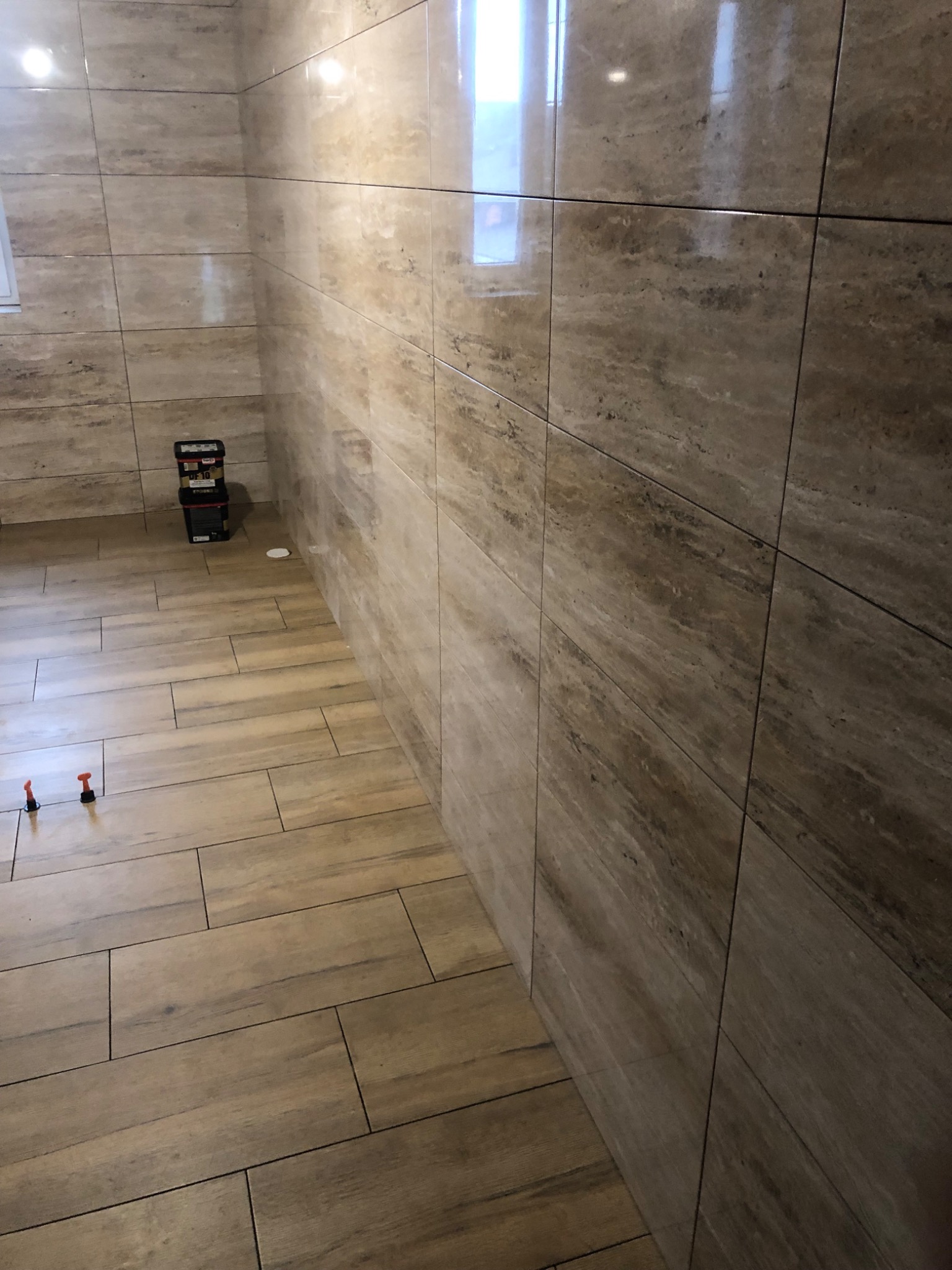 Ukończona łazienka z beżowymi płytkami imitującymi drewno na podłodze i ścianach, widoczne narzędzia glazurnicze na podłodze.