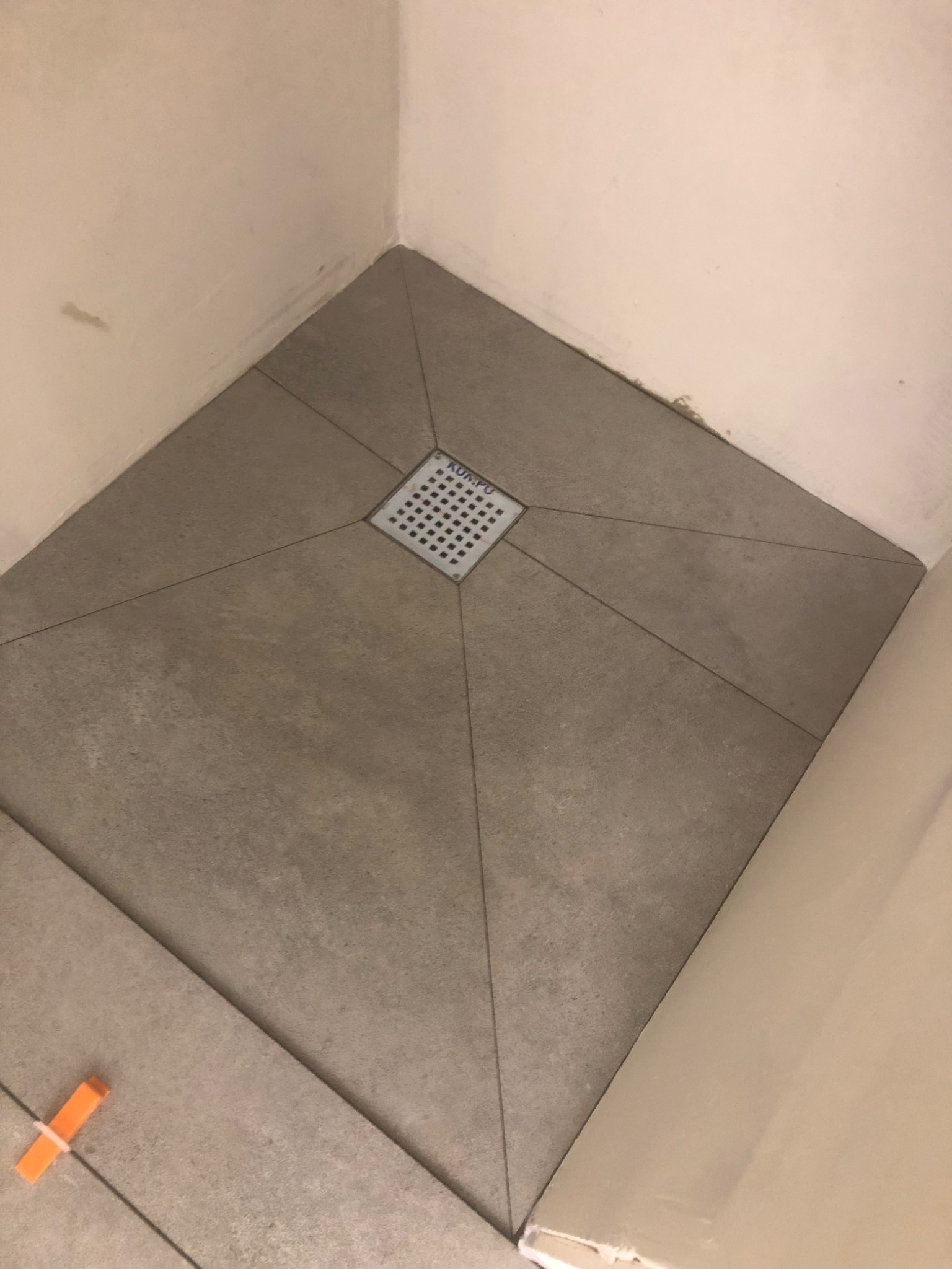 Ułożona podłoga w kabinie prysznicowej z odpływem liniowym w centralnej części i pomarańczowym krzyżykiem dystansowym.