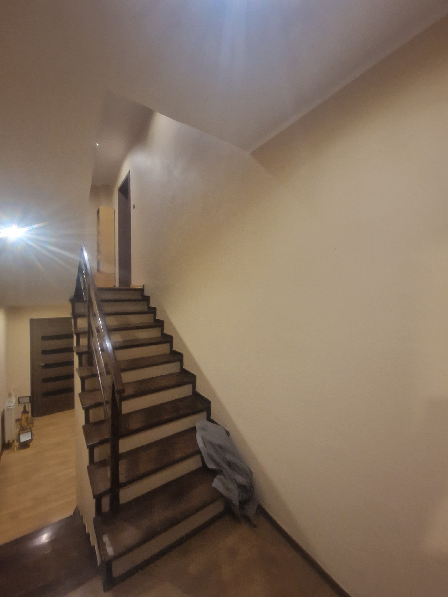 Klatka schodowa z drewnianymi stopniami i balustradą w domu w Bojszowach, częściowo zakryta folią ochronną, ściany przygotowane do malowania.