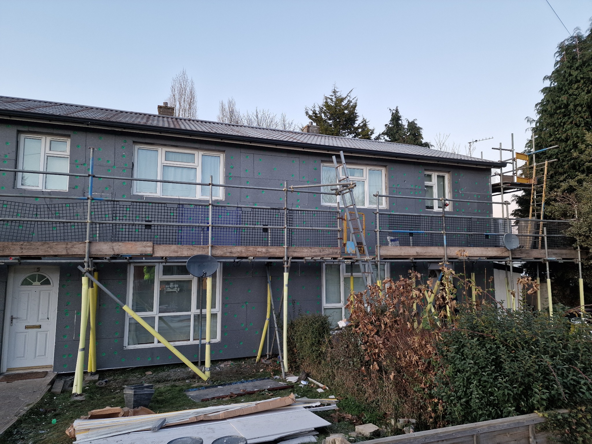 Dom w trakcie ocieplania elewacji, widoczne rusztowania i płyty izolacyjne z charakterystycznymi zielonymi kołkami. Etap prac przed nałożeniem tynku.