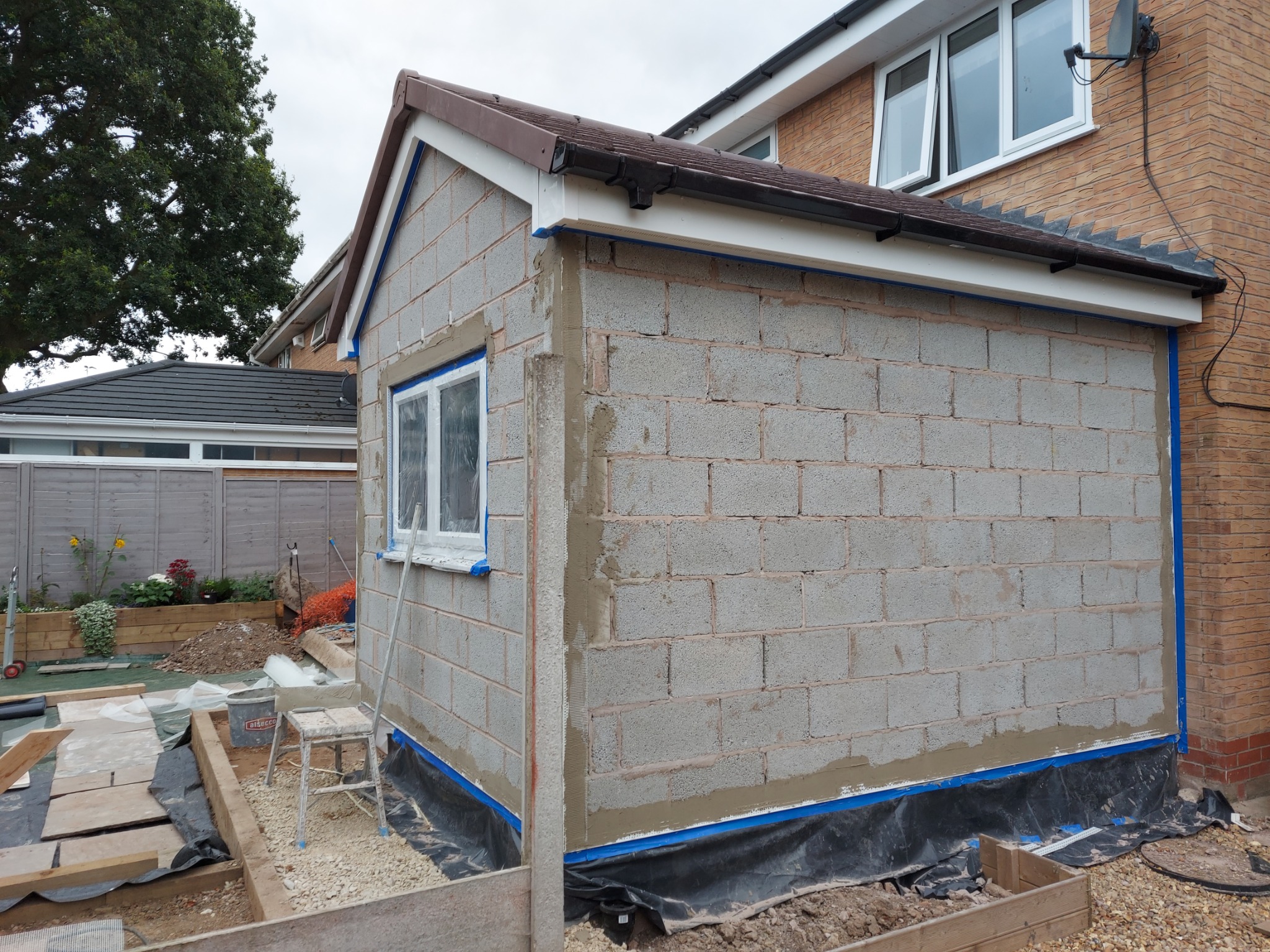 Murowana ściana budynku w Stoke-on-Trent w trakcie prac elewacyjnych; widoczne bloczki, okno zabezpieczone folią i przygotowane podłoże.