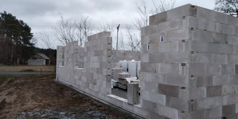 Wznoszenie ścian parterowego domu z betonu komórkowego Ytong, widoczne bloczki z oznaczeniem '600' na szarej, pochmurnej scenerii budowy.