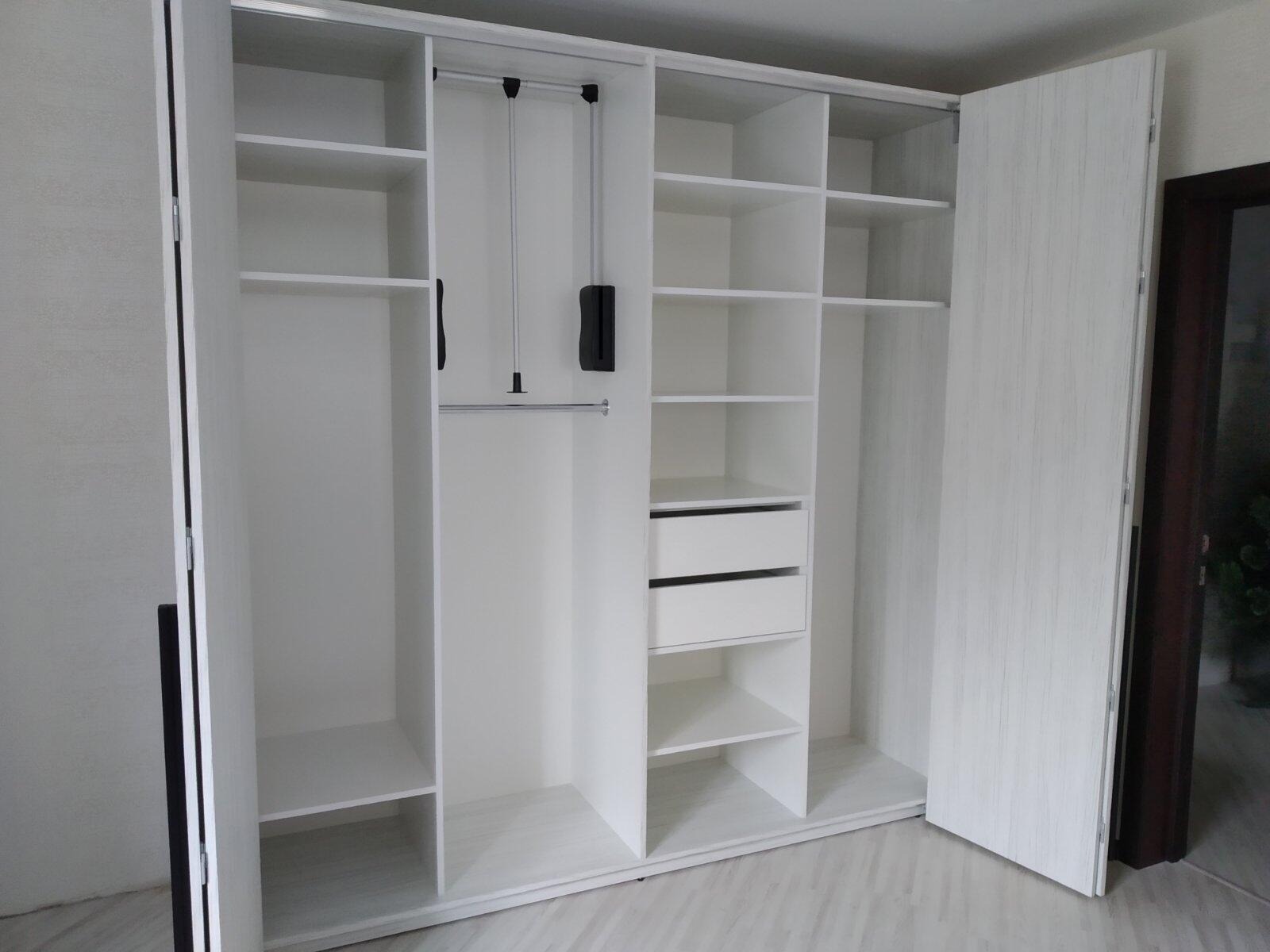 Wnętrze białej, trzydrzwiowej szafy przesuwnej z półkami, szufladami i drążkiem na ubrania, widoczny mechanizm opuszczania drążka.