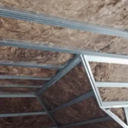 Ocieplenie poddasza wełną mineralną, widoczne metalowe profile konstrukcyjne sufitu podwieszanego.