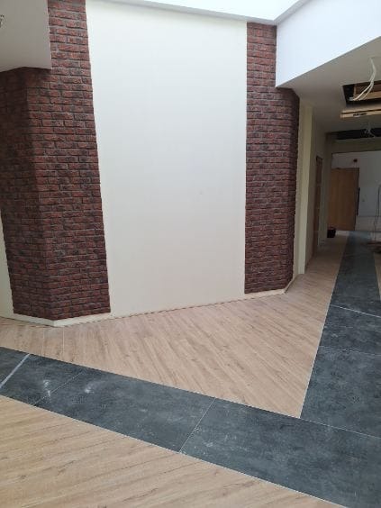 Wnętrze po remoncie: ściany z białym tynkiem i dekoracyjną okładziną z cegły, podłoga wyłożona panelami imitującymi drewno i ciemnymi płytkami. Widoczny fragment sufitu z oknem dachowym.
