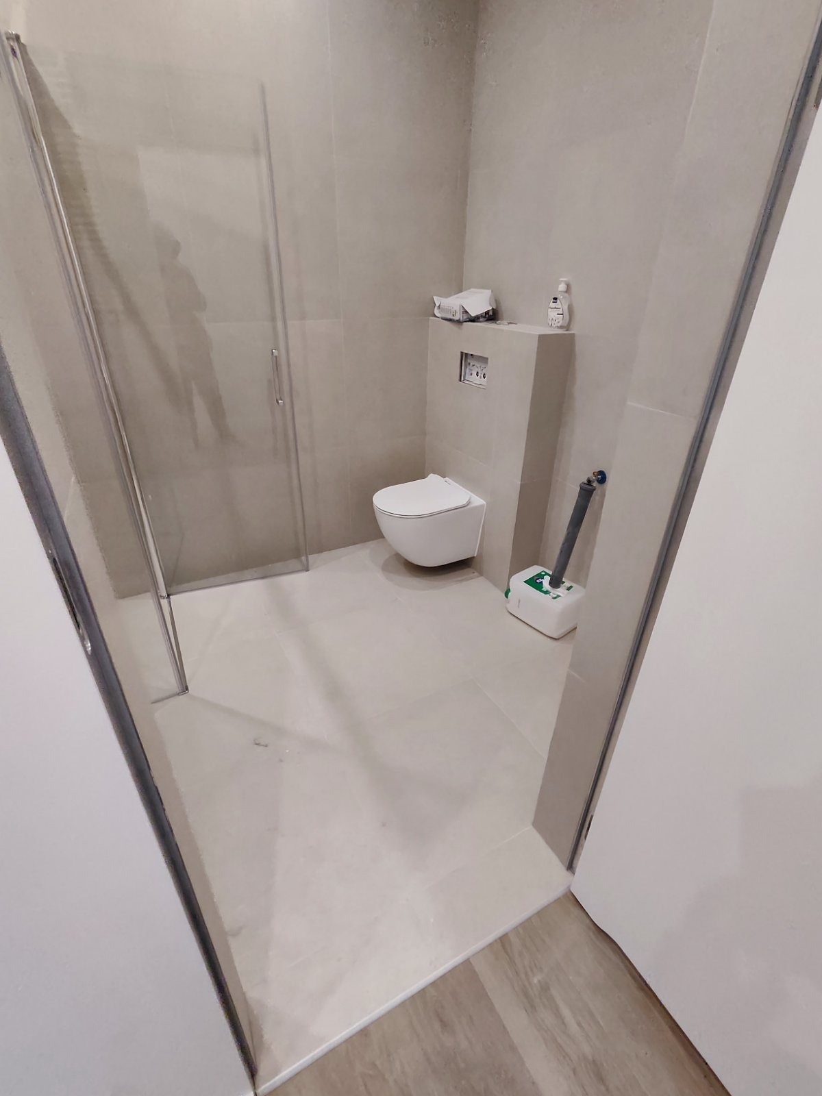 Wykończona łazienka w Warszawie z kabiną prysznicową, podwieszaną toaletą i szarą pompą sanitarną przy ścianie.