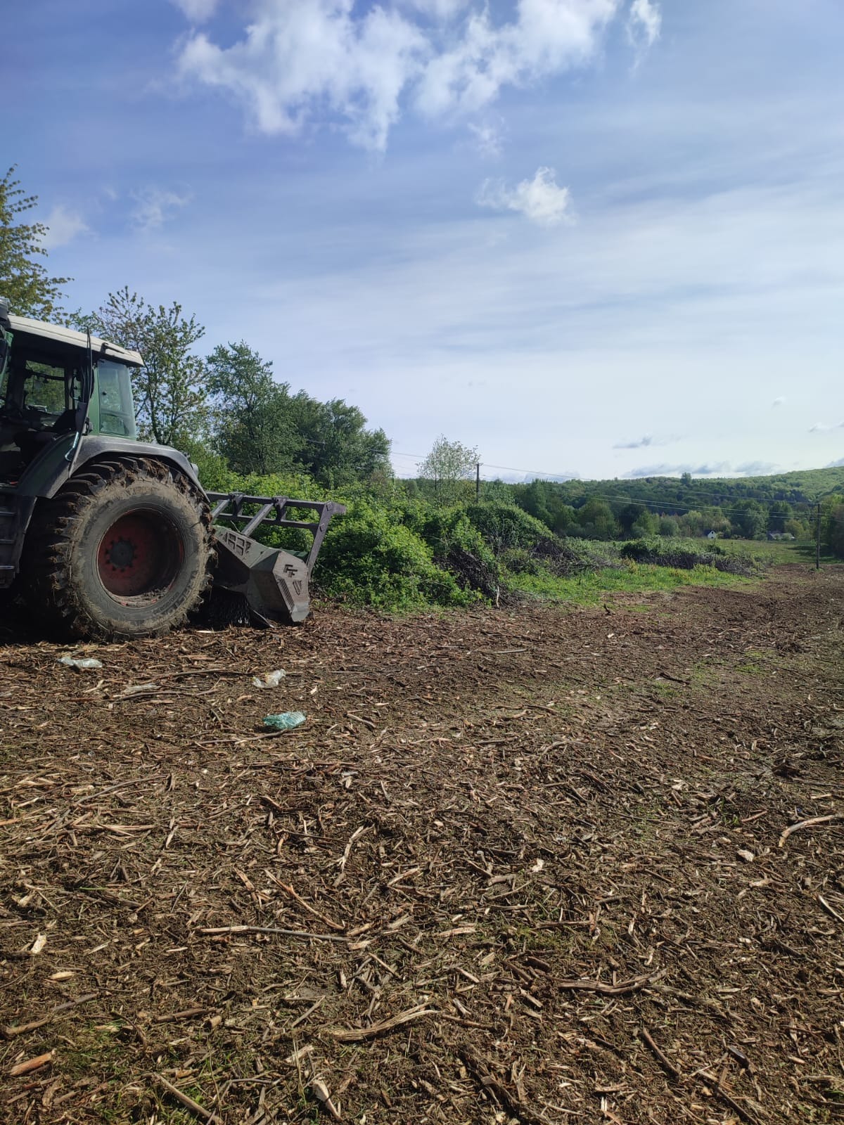 Teren po karczowaniu w Wieliczce, widoczny traktor z osprzętem do mulczowania i pozostałości po wycince w postaci zrębków.