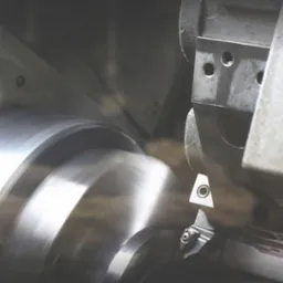 Metalowy element obrabiany na tokarce, widoczne wi&oacute;ry i narzędzie skrawające w trakcie pracy.