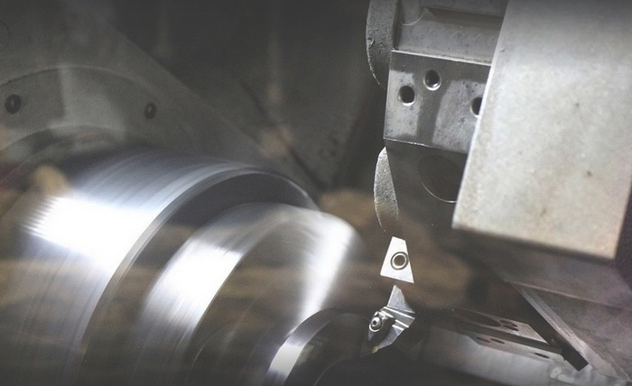 Dynamiczne ujęcie procesu toczenia metalu, z widocznym wiórem i ostrzem tokarskim w zbliżeniu, ukazującym precyzję obróbki.