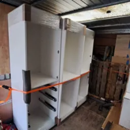 Wnętrze furgonetki z zabezpieczonymi, owiniętymi folią i spiętymi pomarańczowymi pasami szafkami kuchennymi z szufladami, gotowymi do transportu.