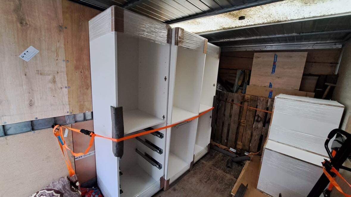 Wnętrze furgonetki z zabezpieczonymi, owiniętymi folią i spiętymi pomarańczowymi pasami szafkami kuchennymi z szufladami, gotowymi do transportu.