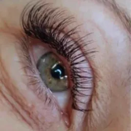 Zbliżenie na oko z zieloną tęczówką i przedłużonymi, gęstymi, ciemnymi rzęsami w stylu 'kocie oko'.