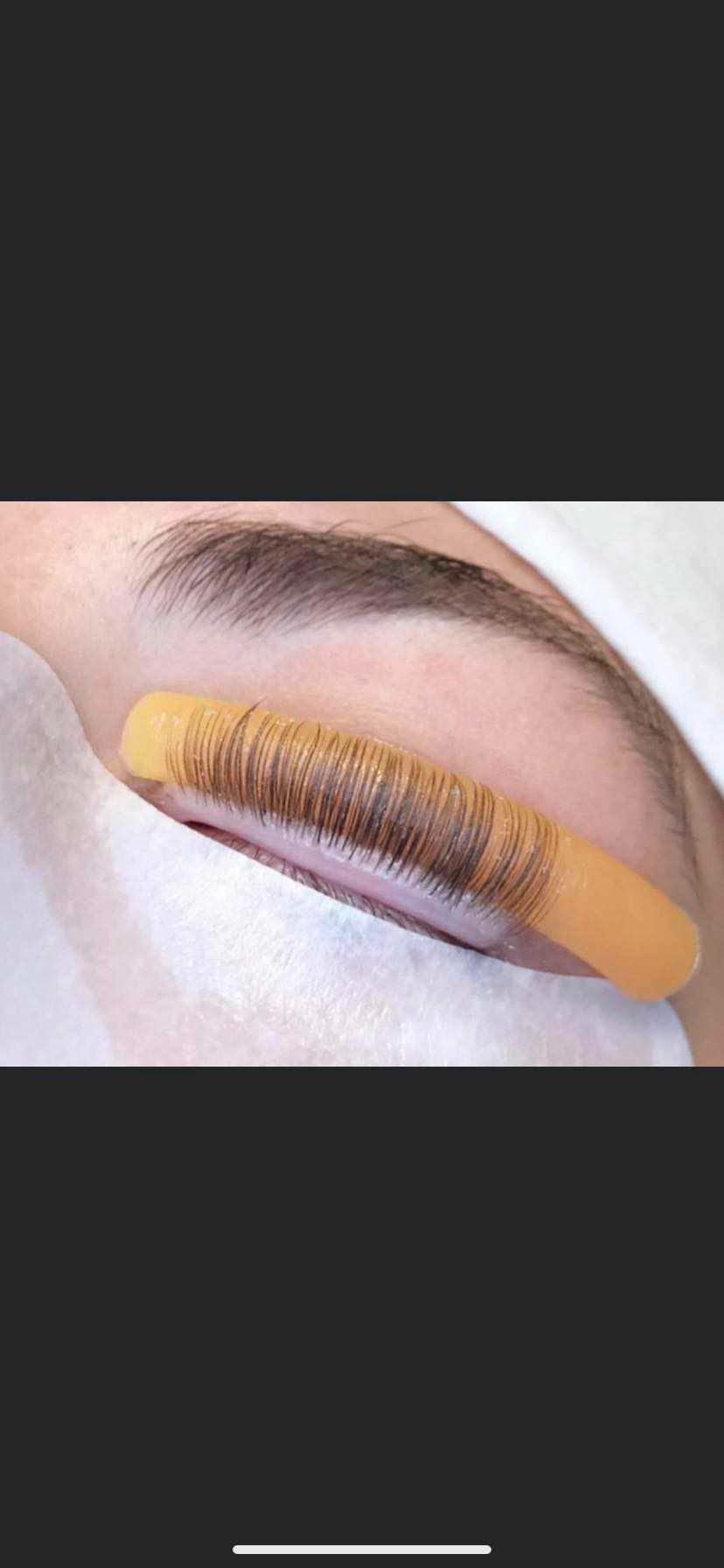 Podkręcanie rzęs za pomocą żółtej formy silikonowej, widoczne brązowe rzęsy na białym podkładzie kosmetycznym, zbliżenie na oko.