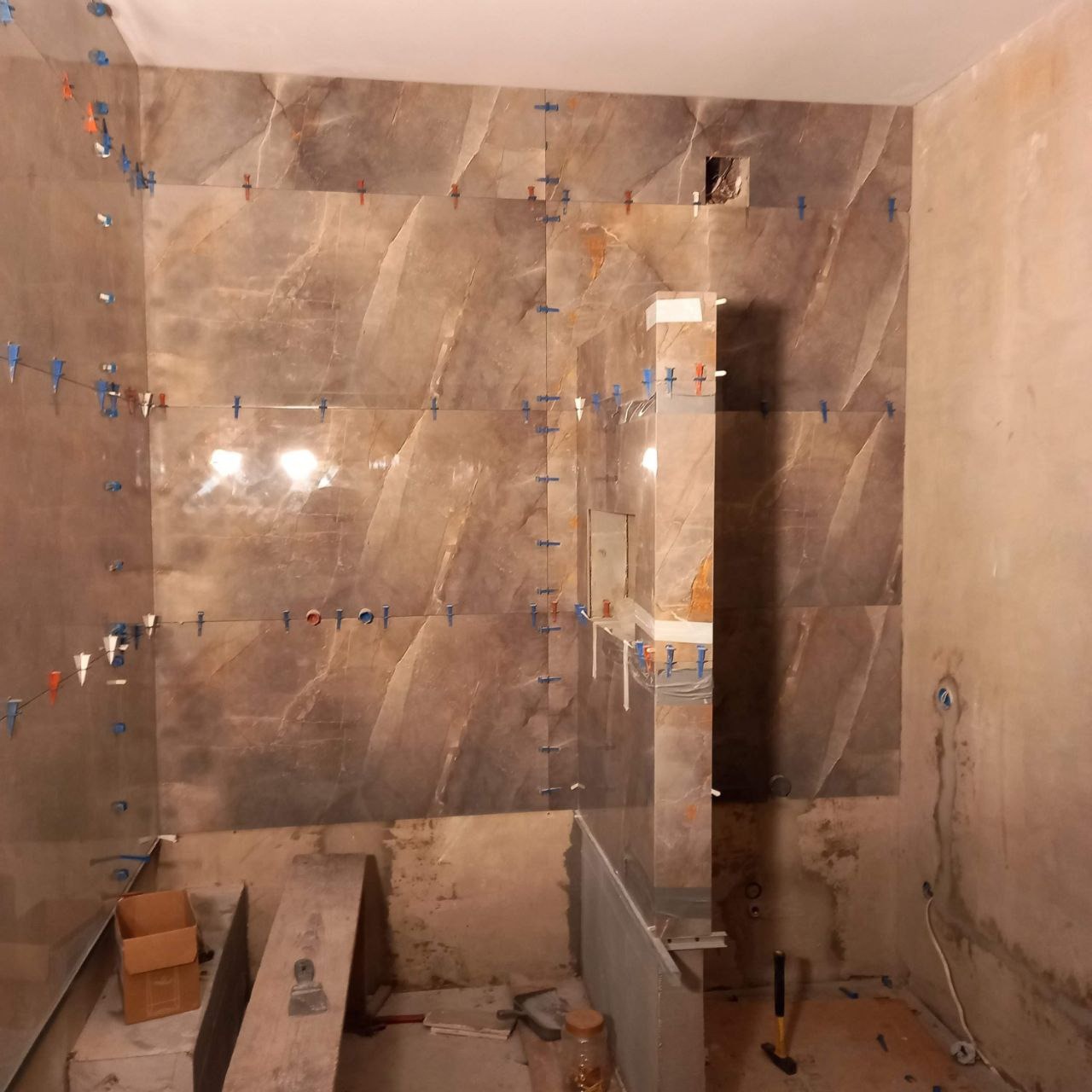 Montaż płytek imitujących marmur w łazience, widoczne niezagruntowane ściany, krzyżyki dystansowe i poziomica.