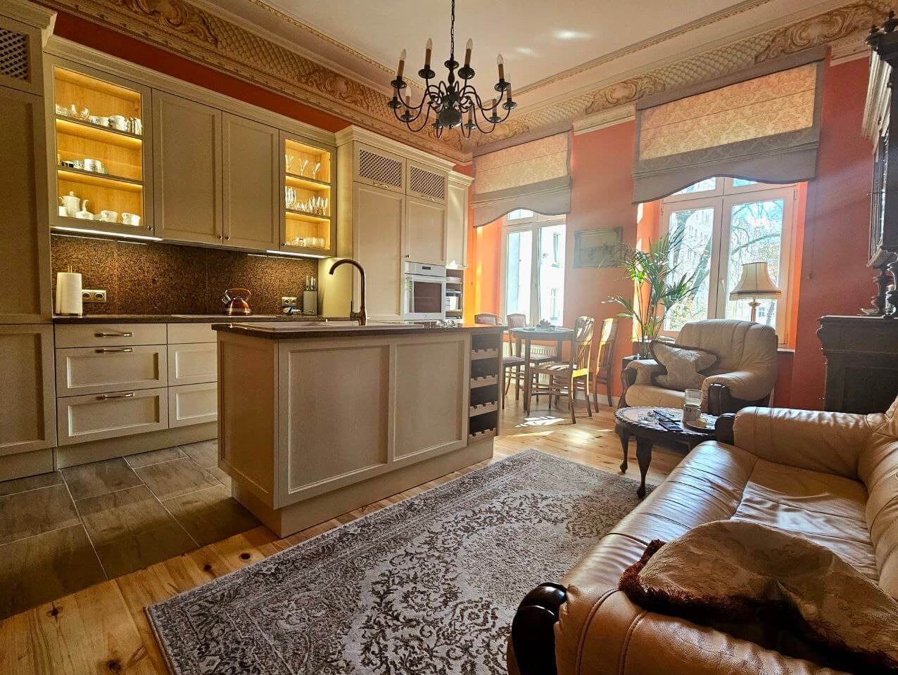 Elegancka kuchnia z wyspą, beżowe szafki z podświetleniem, marmurowy blat i klasyczny dywan w przestronnym wnętrzu z elementami retro.