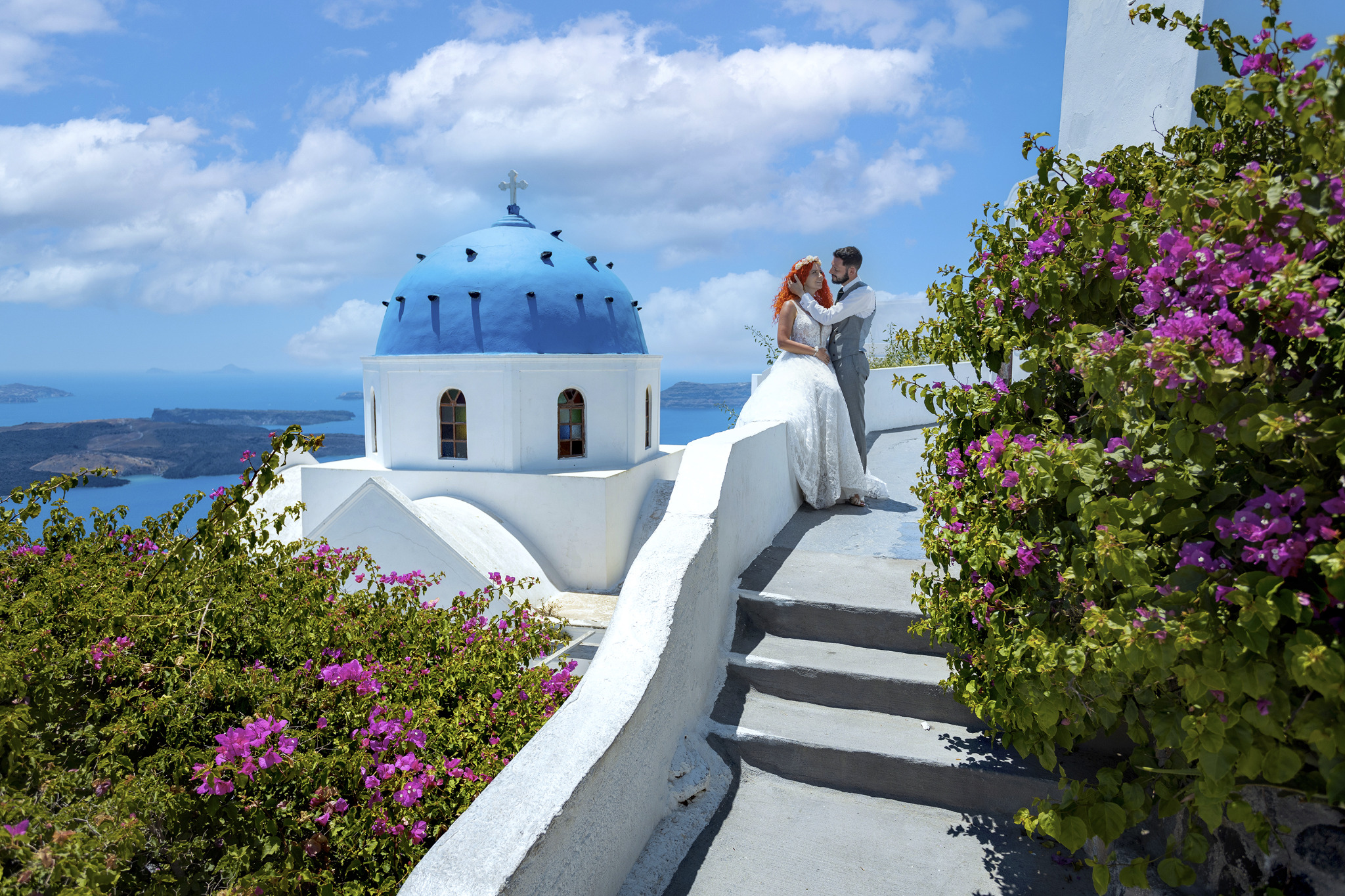 Para młoda na tle białej architektury z niebieską kopułą i widokiem na morze w Santorini, Grecja, otoczona kwitnącymi bugenwillami.