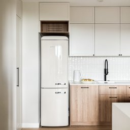 Margareta Gulczyńska GUMA Studio Projektowania Wnętrz - Jasna kuchnia: białe szafki górne i drewniane dolne, retro lodówka Gorenje, czarna bateria, płytki typu cegiełka. Minimalistyczny design z dbałością o detale.