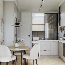 Margareta Gulczyńska GUMA Studio Projektowania Wnętrz - Jasna kuchnia z okrągłym stołem i kwiatami, widok na wnękę z miejscem do siedzenia za przesuwnymi drzwiami. Minimalistyczny design, neutralna kolorystyka i kwiatowy motyw na ścianie.