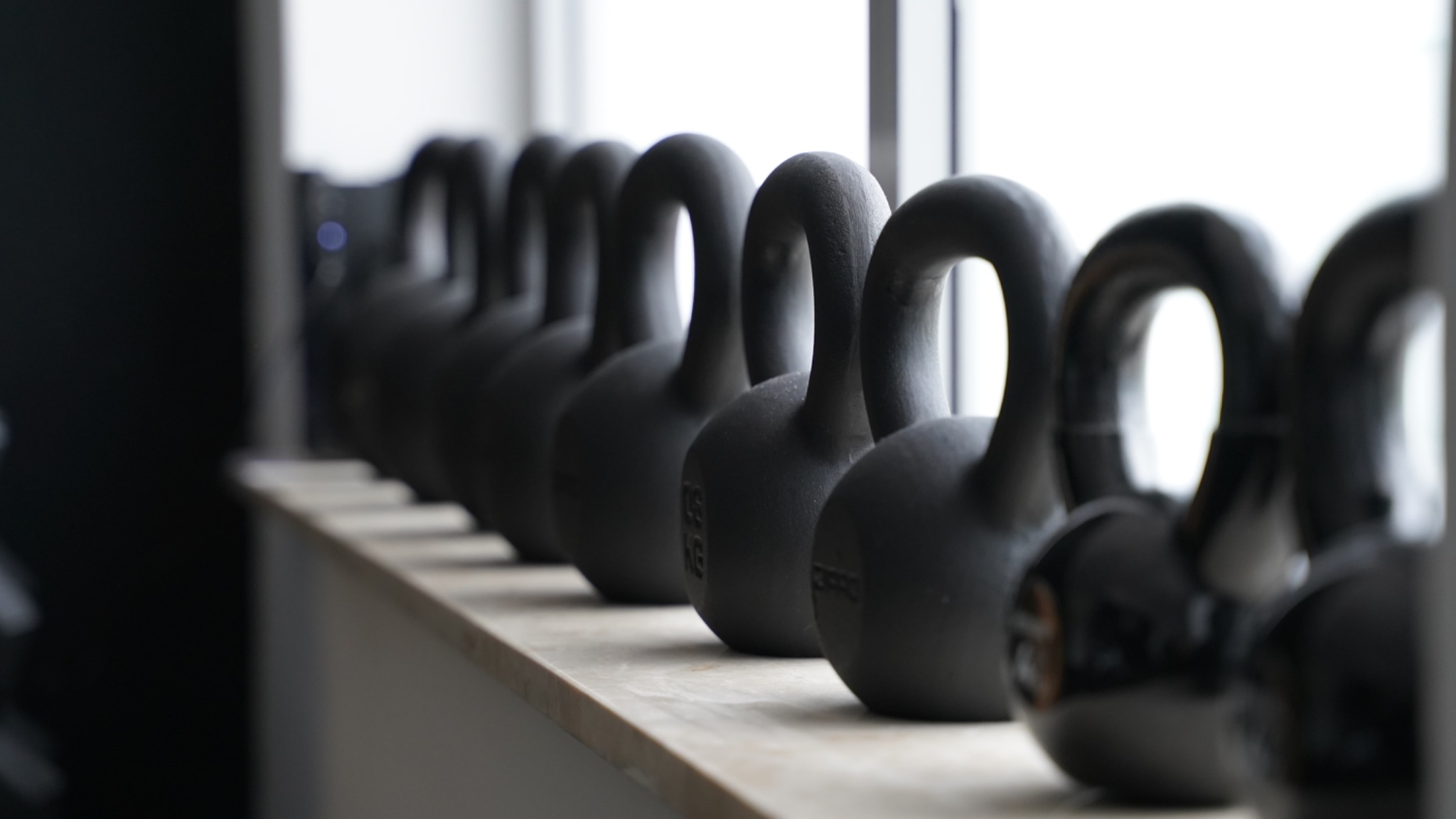 Rząd czarnych kettlebell ustawionych na jasnym parapecie, widoczne z bliska, z delikatnym rozmyciem tła.