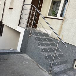 MS WELDER Marcin Skorupski - Zewnętrzne schody z nowoczesną balustradą ze stali nierdzewnej w Stęszewie, prowadzące do drzwi wejściowych. Widoczne szare płytki schodowe i elewacja budynku o jasnej strukturze.