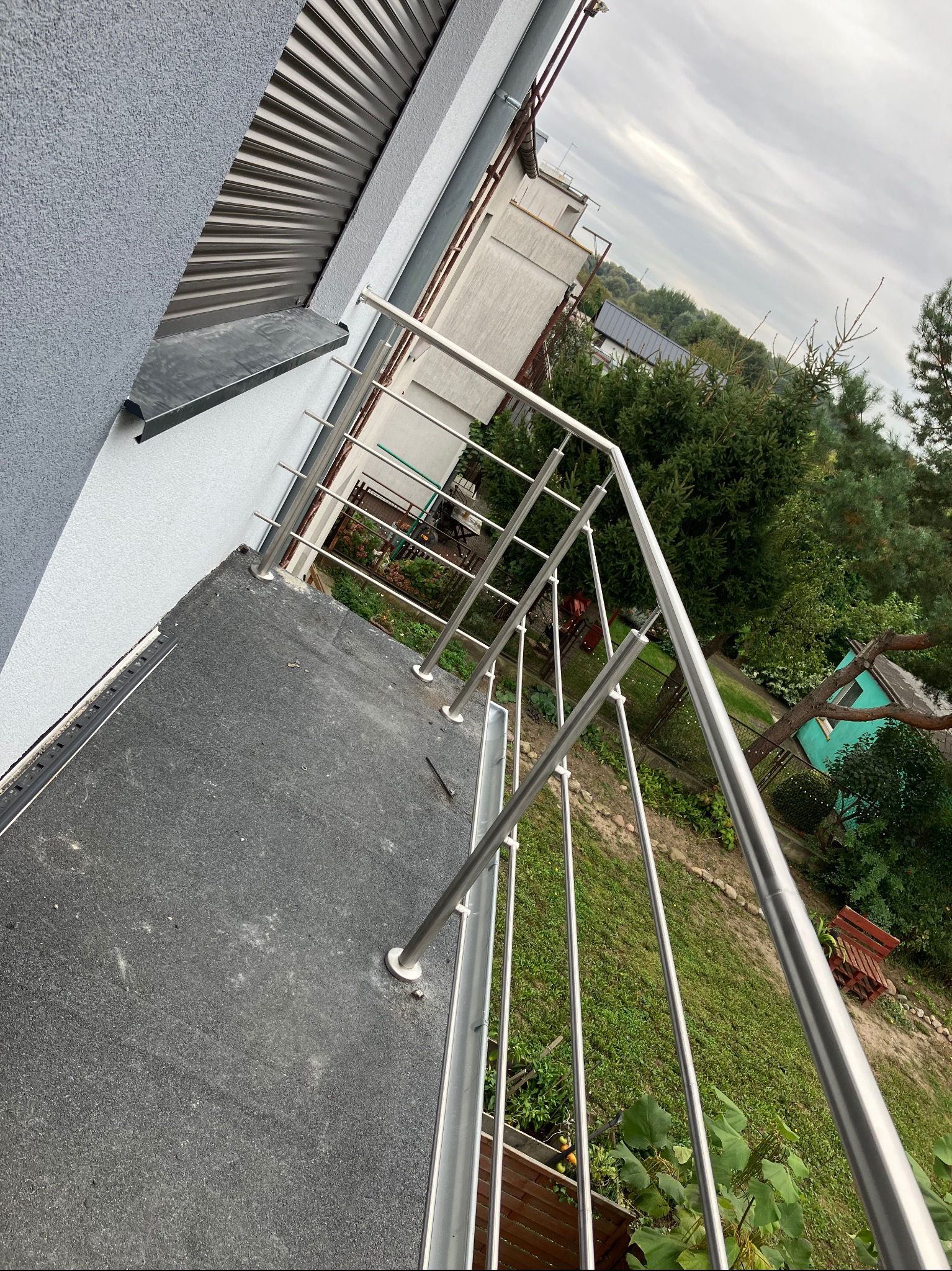 Balkon z zamontowaną, nowoczesną, nierdzewną balustradą w Stęszewie, widok z góry na ogród i sąsiedni budynek.