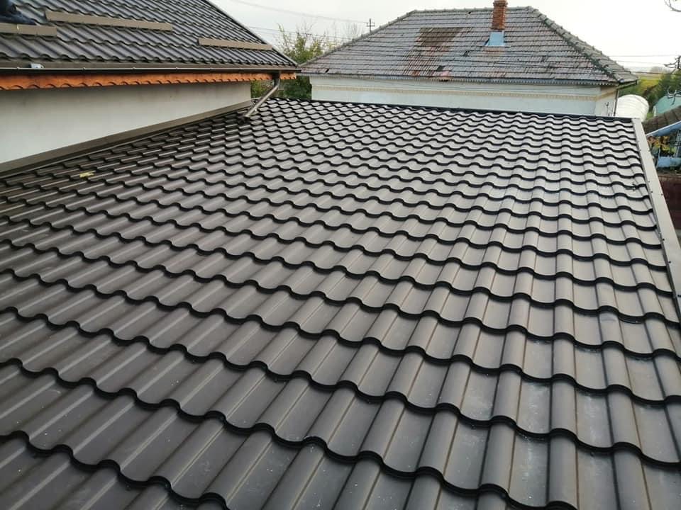 Nowy, ciemnoszary dach z blachy trapezowej na budynku jednorodzinnym, widok z góry, w tle dach sąsiedniego budynku z dachówki ceramicznej.