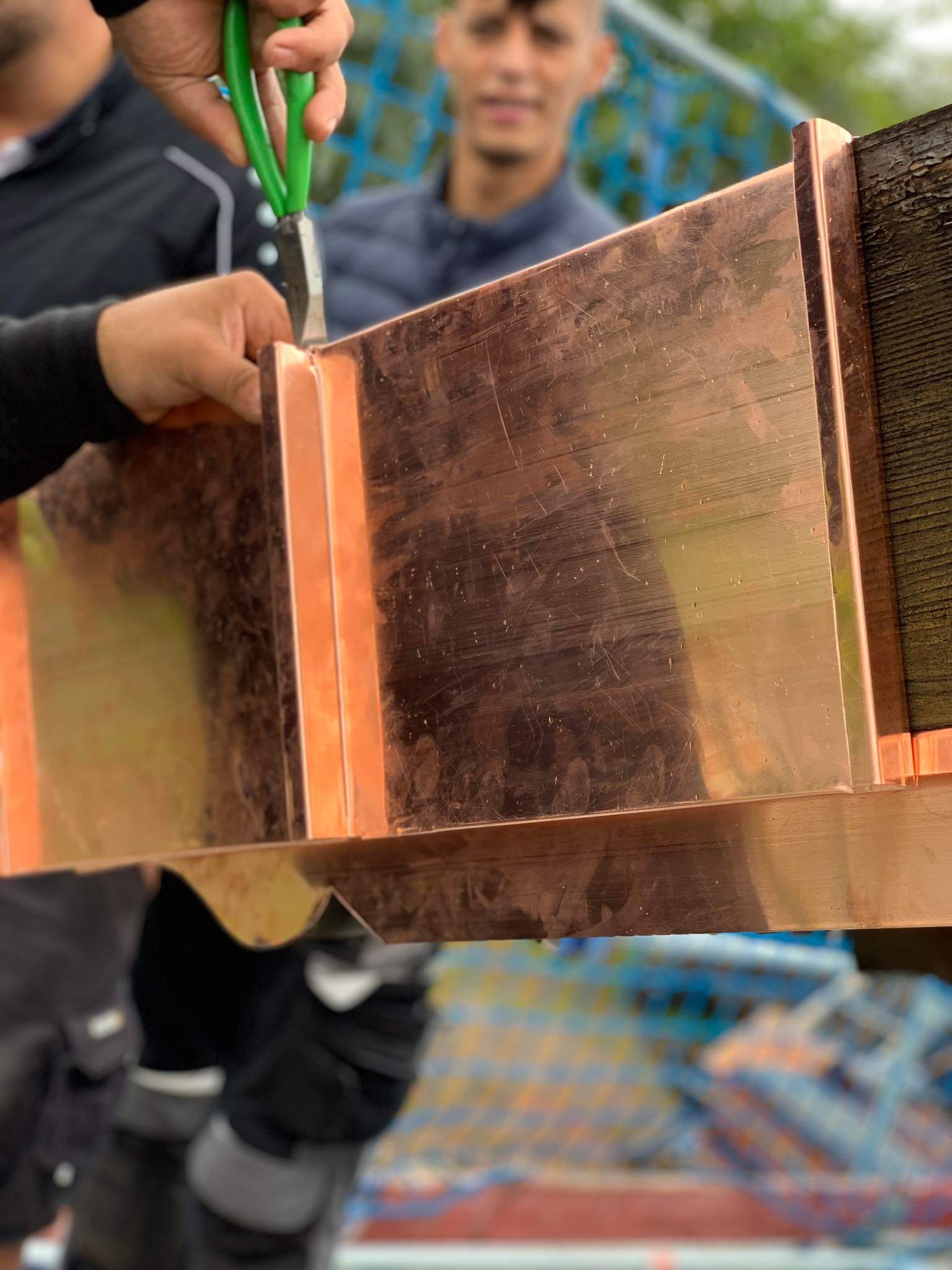 Formowanie miedzianej rynny za pomocą nożyc dekarskich, widoczny fragment dachu i osoba w tle.