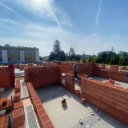 Budowa domu z czerwonej cegły w Częstochowie, widok z góry na ściany fundamentowe i pracownika na tle błękitnego nieba.