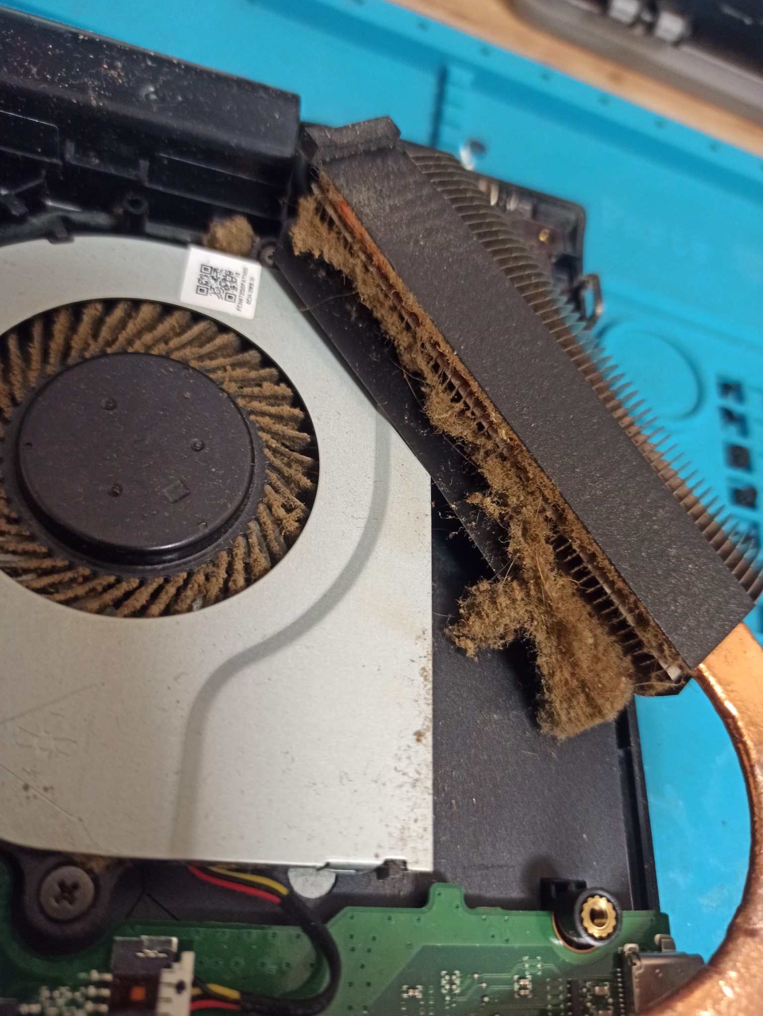 Zanieczyszczony kurzem wentylator i radiator laptopa podczas serwisu, widoczna płyta główna i złącza.