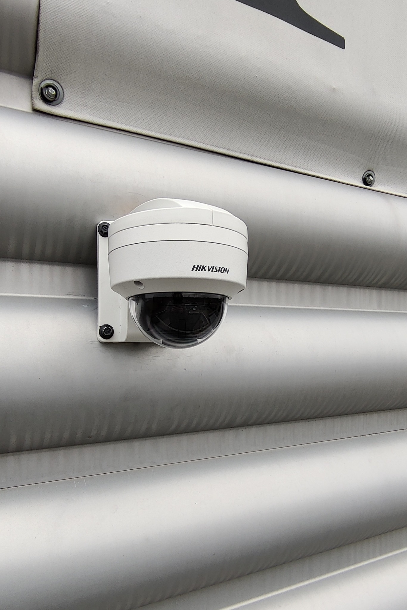 Kamera monitoringu Hikvision, kopułkowa, zamontowana na srebrnej, pofałdowanej elewacji, widok z dołu.