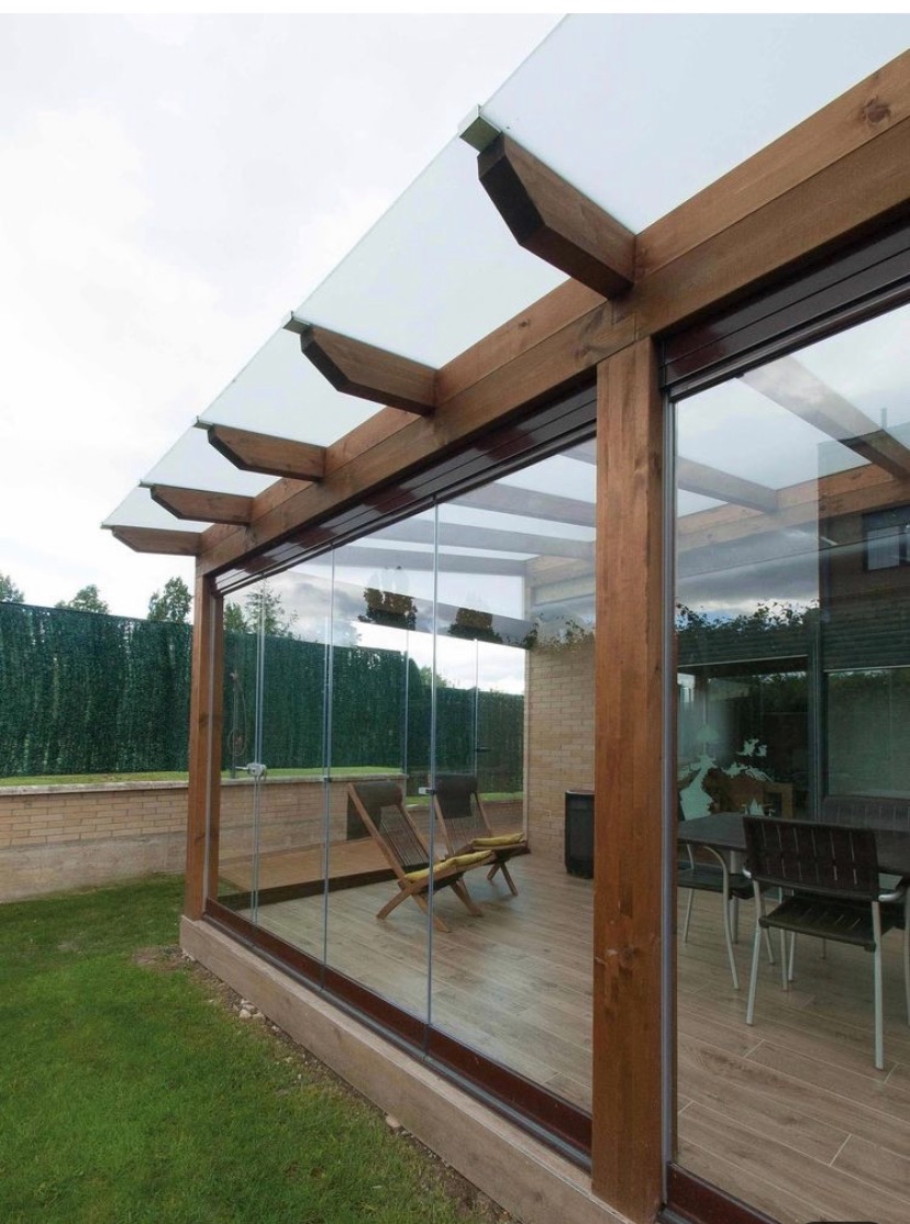 Zadaszony taras z drewnianą konstrukcją, przeszklonymi ścianami przesuwnymi i widocznym ogrodem w tle.