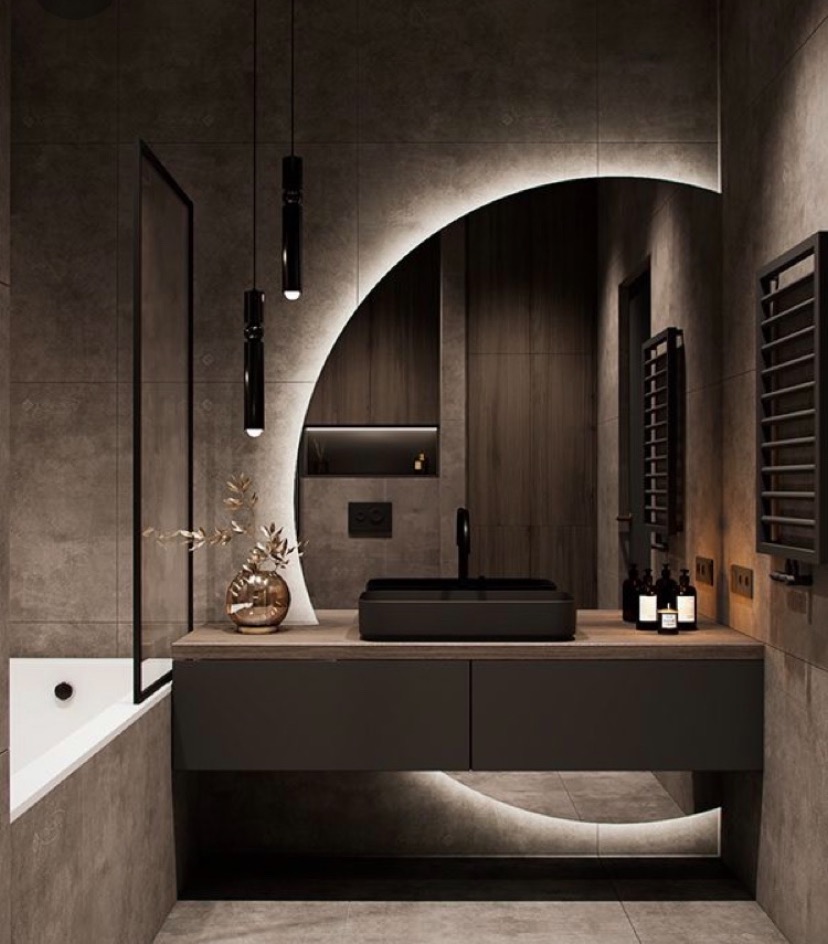 Nowoczesna łazienka z podświetlanym lustrem w kształcie półksiężyca, czarną umywalką nablatową i minimalistyczną armaturą, uzupełniona o wiszące lampy w kształcie tub oraz grzejnik drabinkowy.