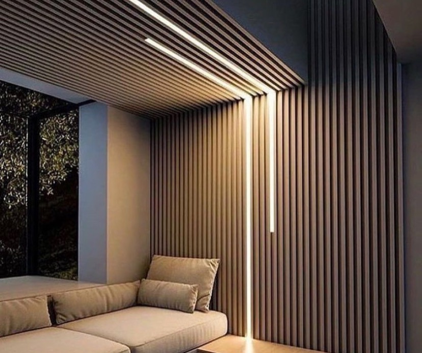 Nowoczesne wnętrze z drewnianą ścianą i sufitem z listew, podświetlonych pionowymi i poziomymi liniami LED, z narożną sofą w neutralnym kolorze.