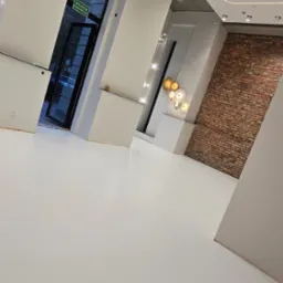 Jasne, przestronne wnętrze z białą posadzką żywiczną, ceglaną ścianą akcentującą, nowoczesnym oświetleniem sufitowym LED i minimalistycznymi dekoracjami ściennymi.