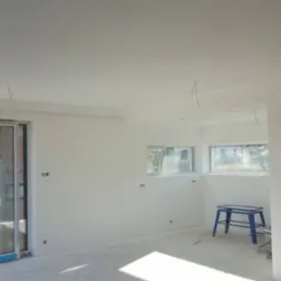 Wnętrze nowo wykończonego pokoju z białymi ścianami, widoczne wystające kable elektryczne i niebieski taboret.