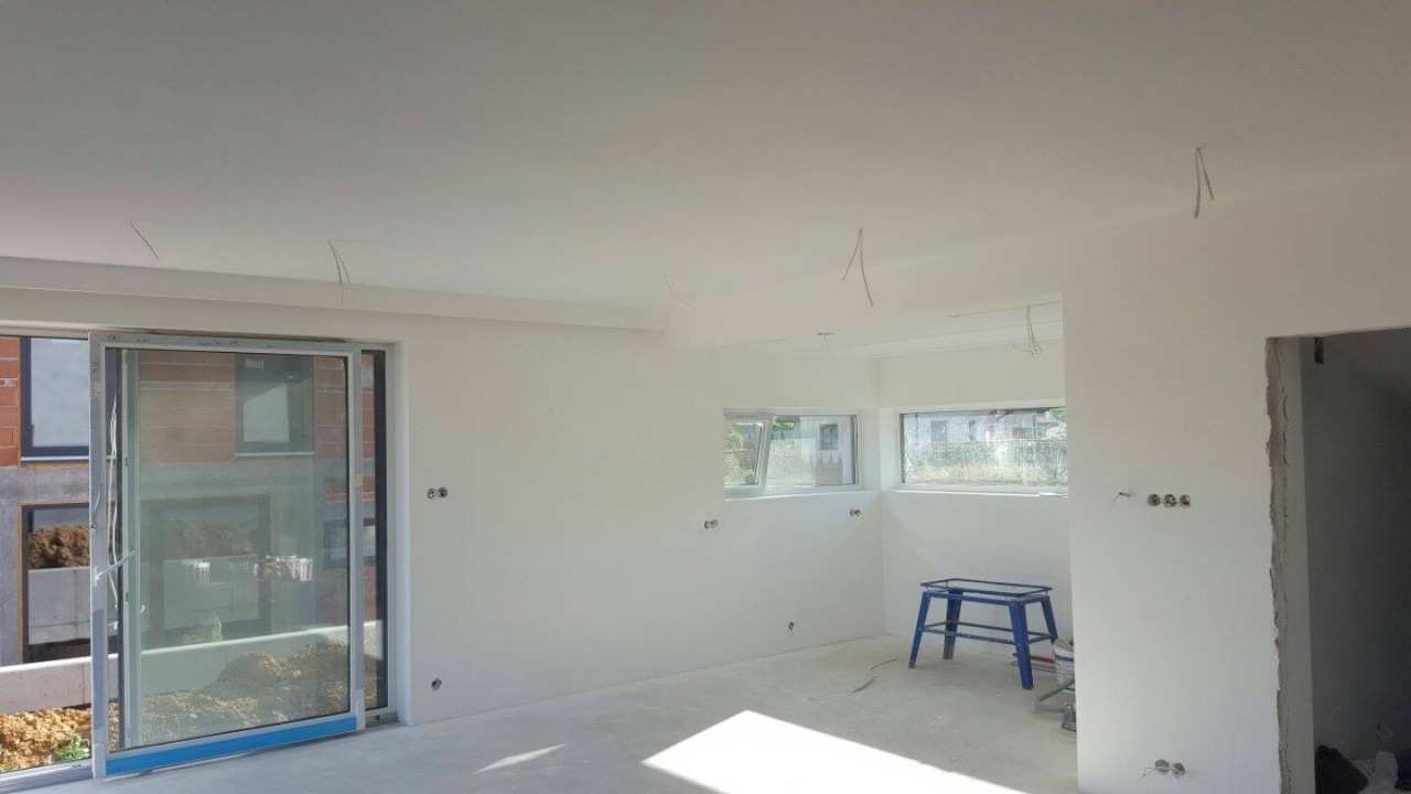 Wnętrze nowo wykończonego pokoju z białymi ścianami, widoczne wystające kable elektryczne i niebieski taboret.