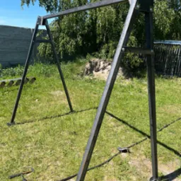 Surowa, metalowa konstrukcja huśtawki ogrodowej w trakcie montażu na trawniku, widoczne narzędzia i elementy mocujące.