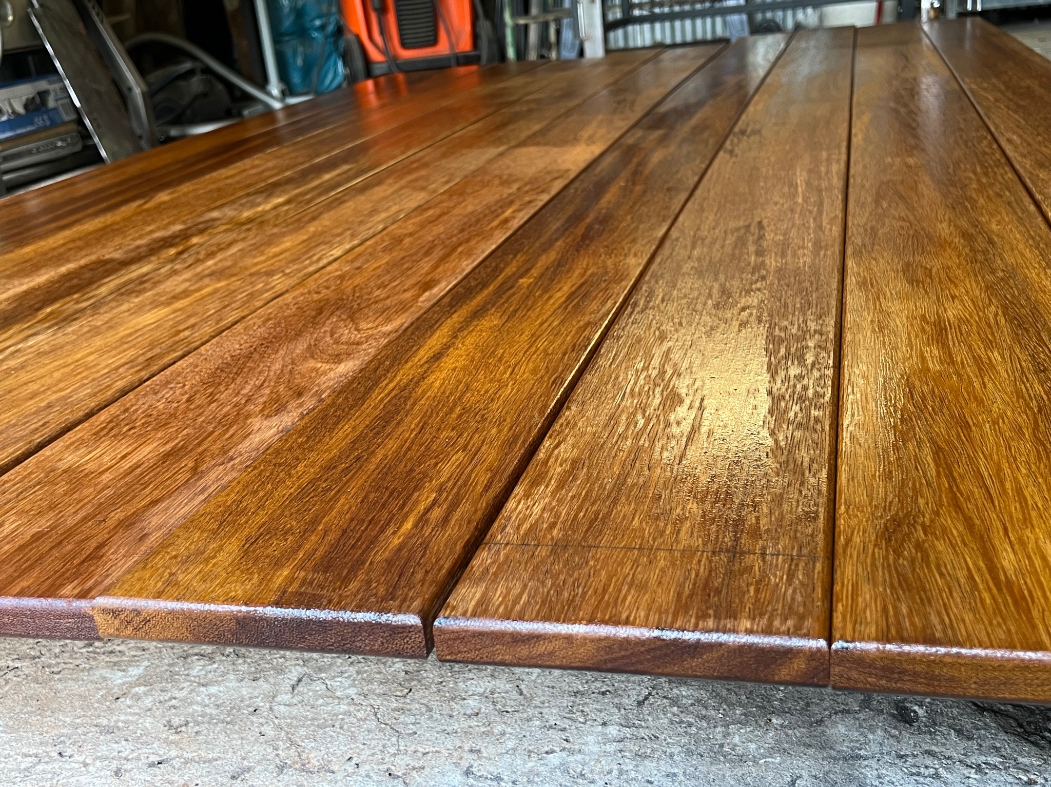 Polerowane, lakierowane deski z ciemnego drewna ułożone obok siebie, tworzące płaską powierzchnię. Widoczne refleksy światła na lakierze i delikatne słoje drewna.