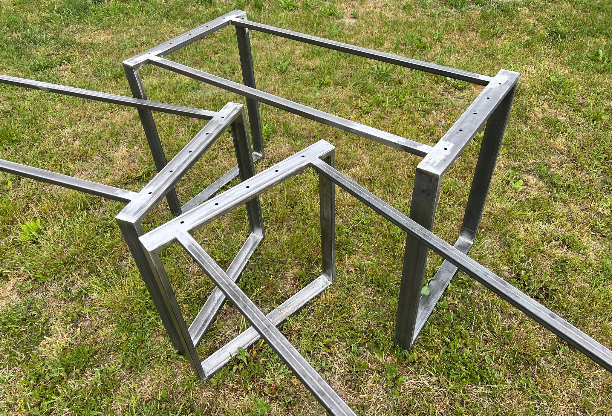 Surowe, metalowe ramy konstrukcyjne z otworami na śruby, leżące na trawie w świetle dziennym.