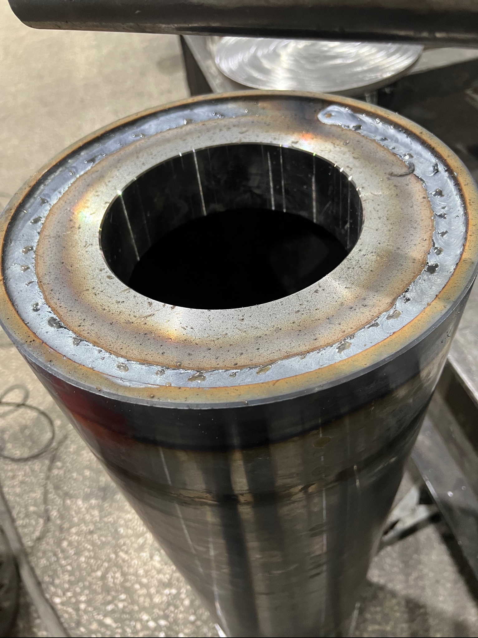 Metalowy cylinder z wyraźnymi śladami spawania na krawędziach, widoczne niedoskonałości spoin i przebarwienia termiczne.