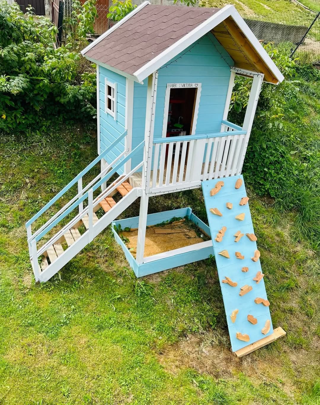 Niebieski domek zabaw dla dzieci z piaskownicą i ścianką wspinaczkową, wykonany w Korzennej, z napisem 'Franek & Wiktoria' nad wejściem.