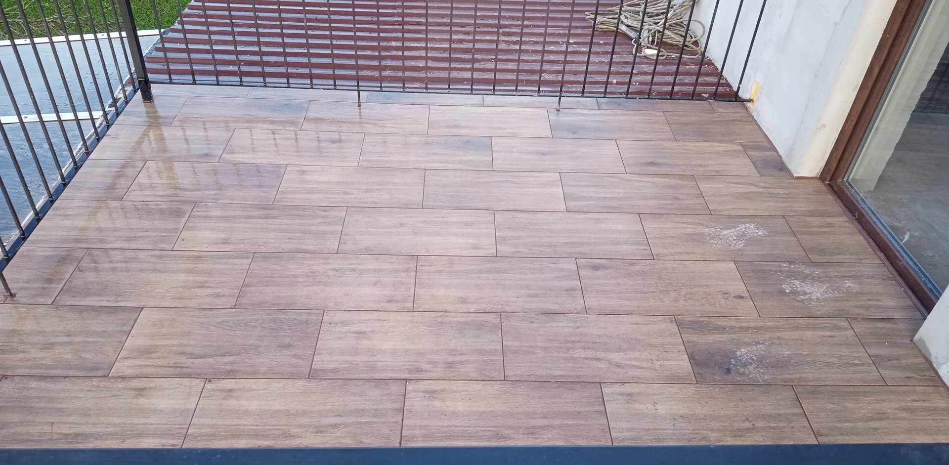 Wyłożony płytkami taras z metalową barierką, widoczne ślady po butach na powierzchni płytek.