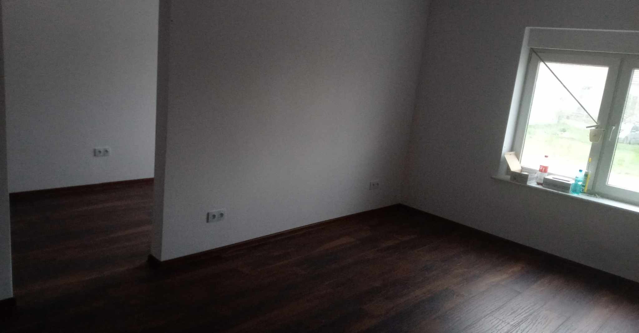 Pusty pokój z ciemną podłogą, świeżo pomalowanymi szarymi ścianami i oknem z widocznymi akcesoriami na parapecie.