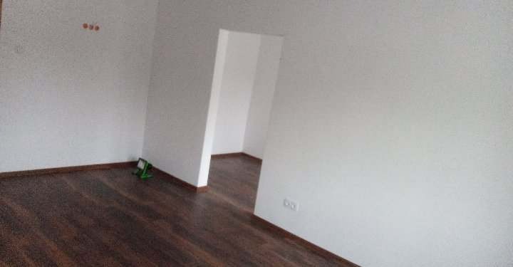 Pomalowane na biało wnętrze pokoju z ciemną podłogą, widoczne gniazdko elektryczne i zielony poziomica laserowa przy ścianie.