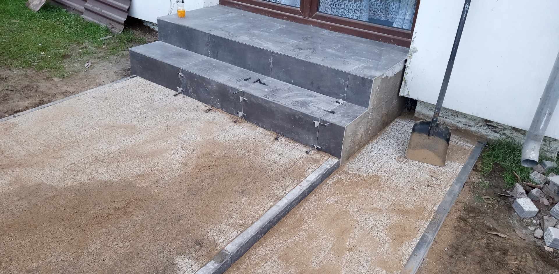 Układanie płytek na schodach wejściowych do domu w Gorzowie Wielkopolskim, widoczne krzyżyki dystansowe i piasek na podłożu.