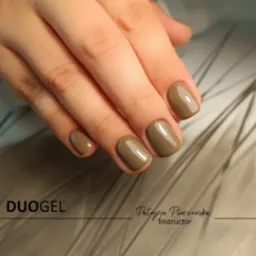 Dłoń z oliwkowymi, błyszczącymi paznokciami o zaokrąglonym kształcie, prezentacja produktu Duogel i nazwiska instruktora Patrycji Pinczewskiej.