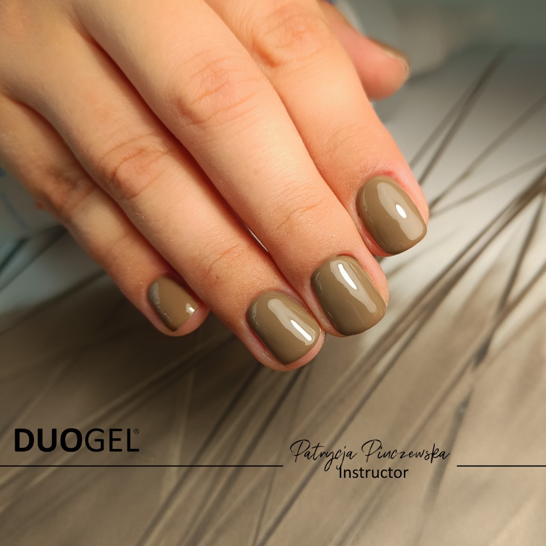 Dłoń z oliwkowymi, błyszczącymi paznokciami o zaokrąglonym kształcie, prezentacja produktu Duogel i nazwiska instruktora Patrycji Pinczewskiej.