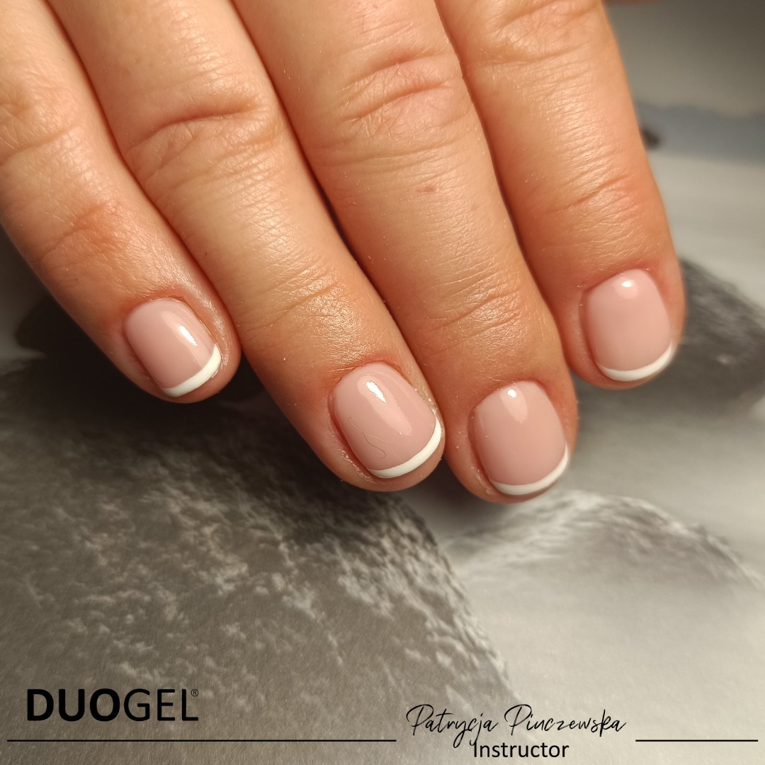 Dłoń z krótkimi, naturalnymi paznokciami w stylu french manicure z wyraźnym, białym paskiem na końcach, na tle z subtelnym wzorem przypominającym marmur. Widoczne logo DUOGEL i podpis Patrycja...