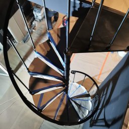 Marta Gałka Usługi - Widok z góry na spiralne schody z metalu, zabezpieczone taśmą malarską przed malowaniem, w trakcie prac wykończeniowych w budynku.