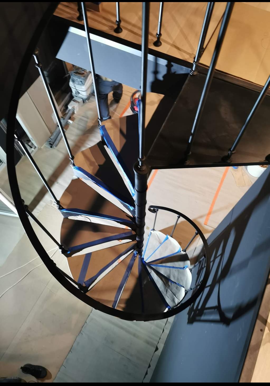 Widok z góry na spiralne schody z metalu, zabezpieczone taśmą malarską przed malowaniem, w trakcie prac wykończeniowych w budynku.